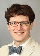 Brian J. Burkett, MD, man wearing glasses and a cream colored suit with a bow tie