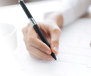 a hand holding a black pen poised to begin writing. background is faded