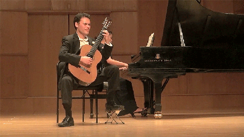 Brandon K.K. Fields on stage playing guitar and accompanied by a pianist