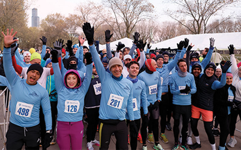 A crowd of runners dressed in cold weather gear hold up five fingers for the RSNA 5k Fun Run