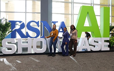 Three women pose in front of the large RSNAI letters in the RSNAI showcase