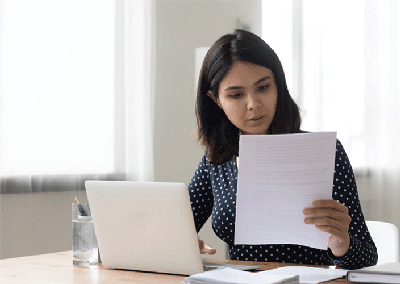 Shutterstock 1916511707 Young person sitting in front of a computer and looking at paperwork