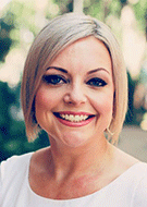 Head shot of Jesse Conyers, MD. Woman with blonde hair smiling. Trees or greenery in the background.