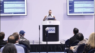 A presenter speaking on stage in the RSNA annual meeting Learning Center Theater