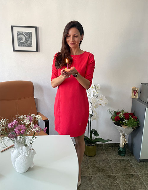 Svetla Dineva, MD, PhD holding a flower. Other bouquets of flowers are in the room on table and floor.
