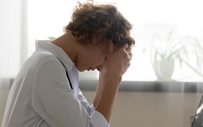 Woman sits in front of a computer, elbows resting on the table and her head in her hands showing distress.