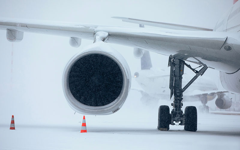 Partial wing and engine of a commercial jet on the ground in snow.