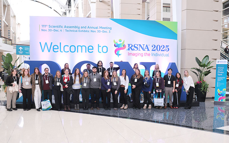 Large group of attendees pose in front of the welcome sign and RSNA letters at RSNA 2025.