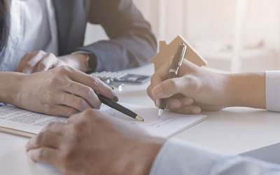Shutterstock image shows the hands of two people in business attire sitting across a table from each other with documents on the tabletop. Each is holding a writing instrument.