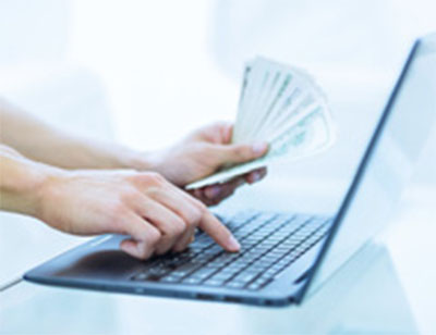 Side view of two hands near laptop with one typing and the other holding paper money fanned out