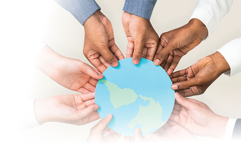 Five sets of hands of a variety of ethnicities hold a paper globe