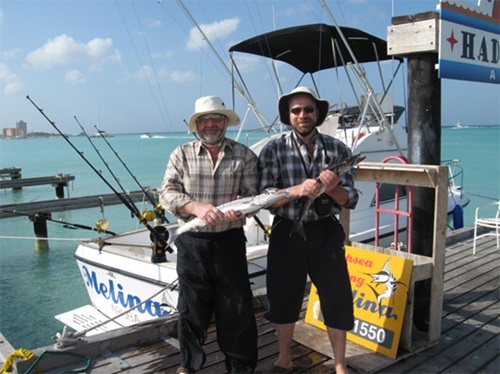 Michael N. Patlas and friend stand on dock wearing fishing attire holding fish