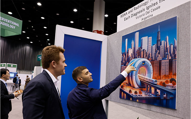Two men dressed in suits look and point at a work of art featuring a large piece of medical imaging equipment set against the backdrop of a city.