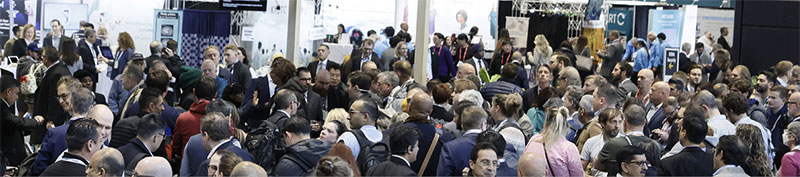 A large crowd of professionals are gathered at a conference in the exhibit hall.