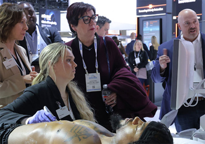 A woman demonstrates an ultrasound procedure on a mannequin before a small group of onlookers.