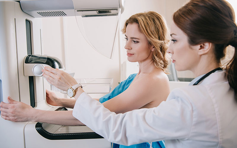 Physician guides a woman who is receiving a mammogram.
