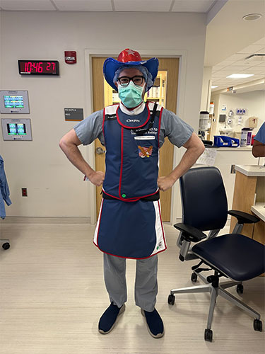 Julius Chapiro, MD, PhD, wears a blue and red cowboy hat, a face mask and a blue and red lead apron. 