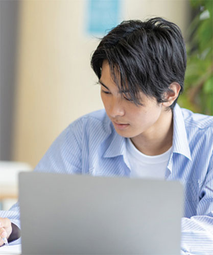 Man in blue and white striped shirt works in front of a laptop. 