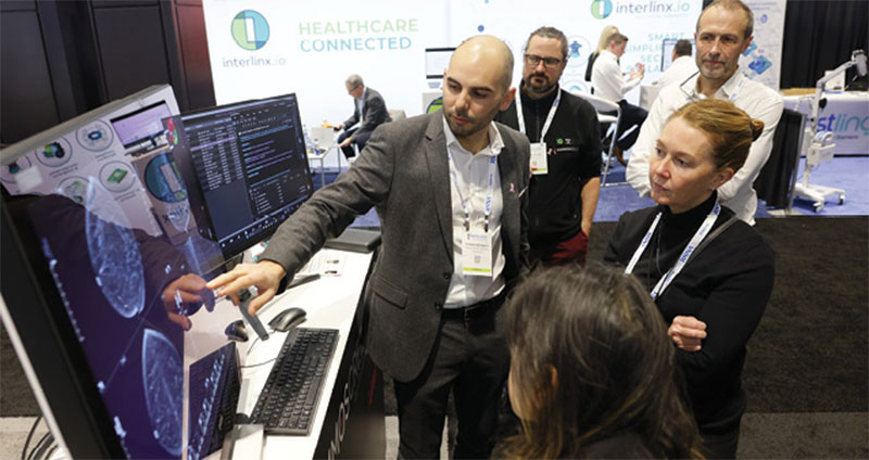 Exhibitors demonstrate medical imaging software on large monitors for attendees gathered at an exhibit hall booth.