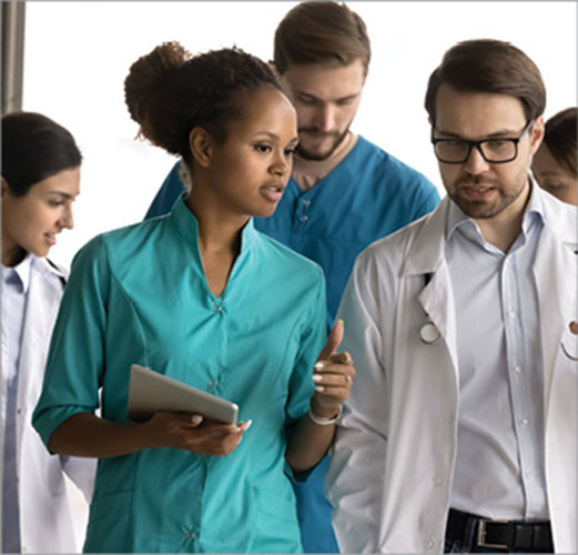 Medical professionals walk together and discuss information while one person carries a tablet.