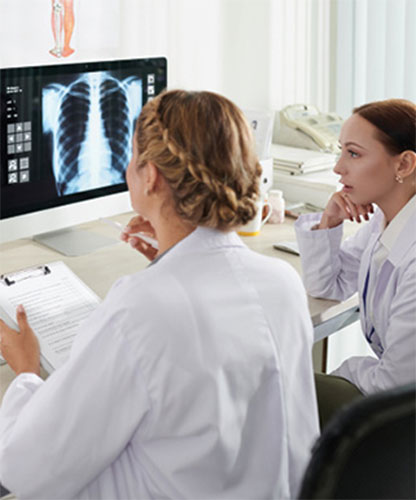 Two healthcare professionals in white coats review a chest X-ray displayed on a computer monitor.