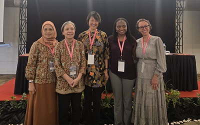 Четыре женщины из числа приглашенных преподавателей RSNA в Индонезии позируют для фотографии перед проекционным экраном.