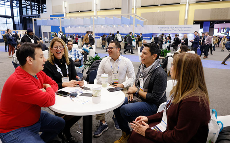 Multicultural group of individuals sits around a table at a conference.