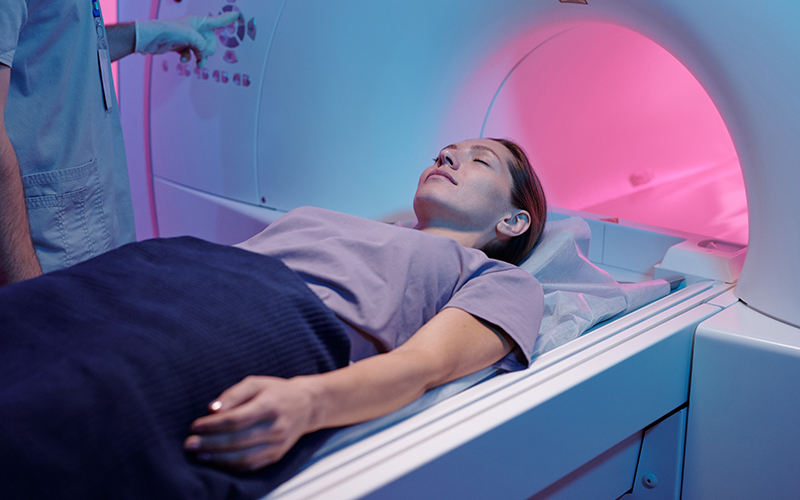 Woman lies with her eyes closed on an MRI table with the MRI opening shown
