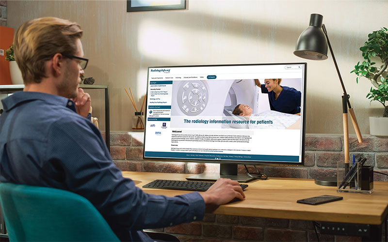 Man sits at a desk looking at a monitor. Radiologyinfo.org is on the screen.