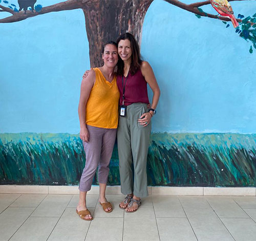 Karen Chetcuti, MBBS, and Katrina McGinty, MD, pose in front of nature mural with a tree where two birds are perched stands surrounded by a grassy field.