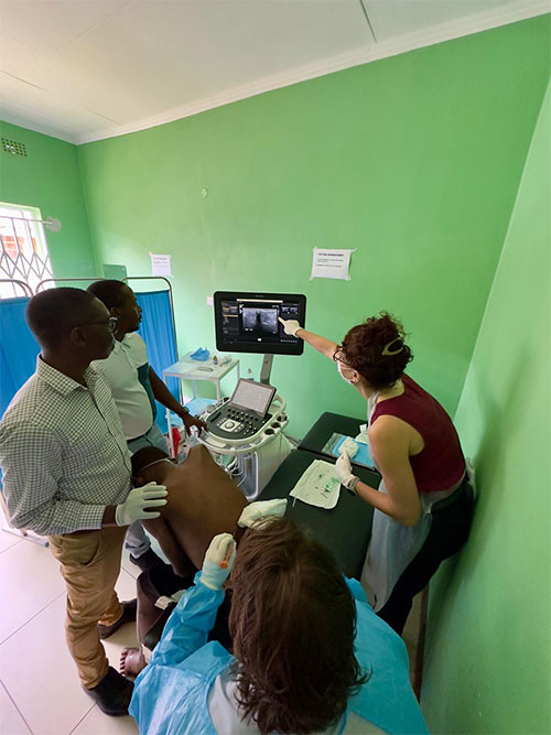 Four medical professionals in a medical setting look at a screen displaying an ultrasound-guided procedure