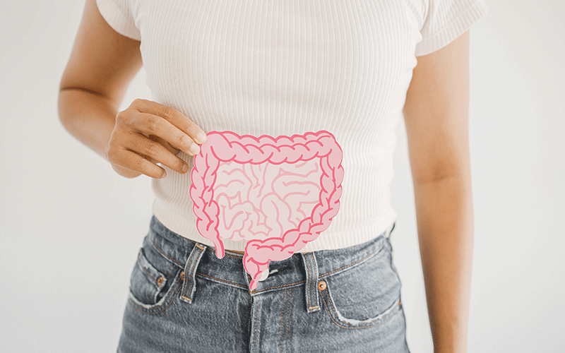 Woman wearing white shirt and jeans holds a drawing of a colon near her abdomen