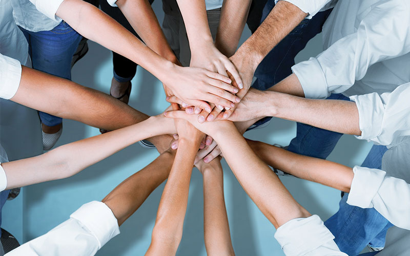 Group of people placing their hands together in a circle to symbolize teamwork and collaboration