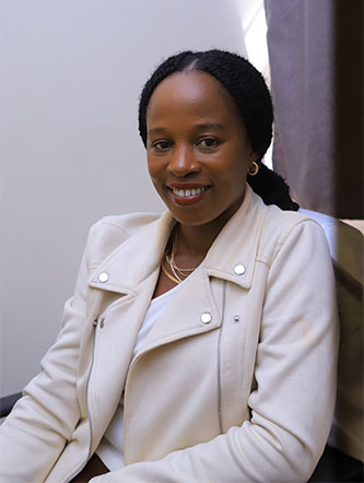 Eva Nabawanuka, MBChB, MMed, EBIR, smiles while sitting while wearing a white jacket. 